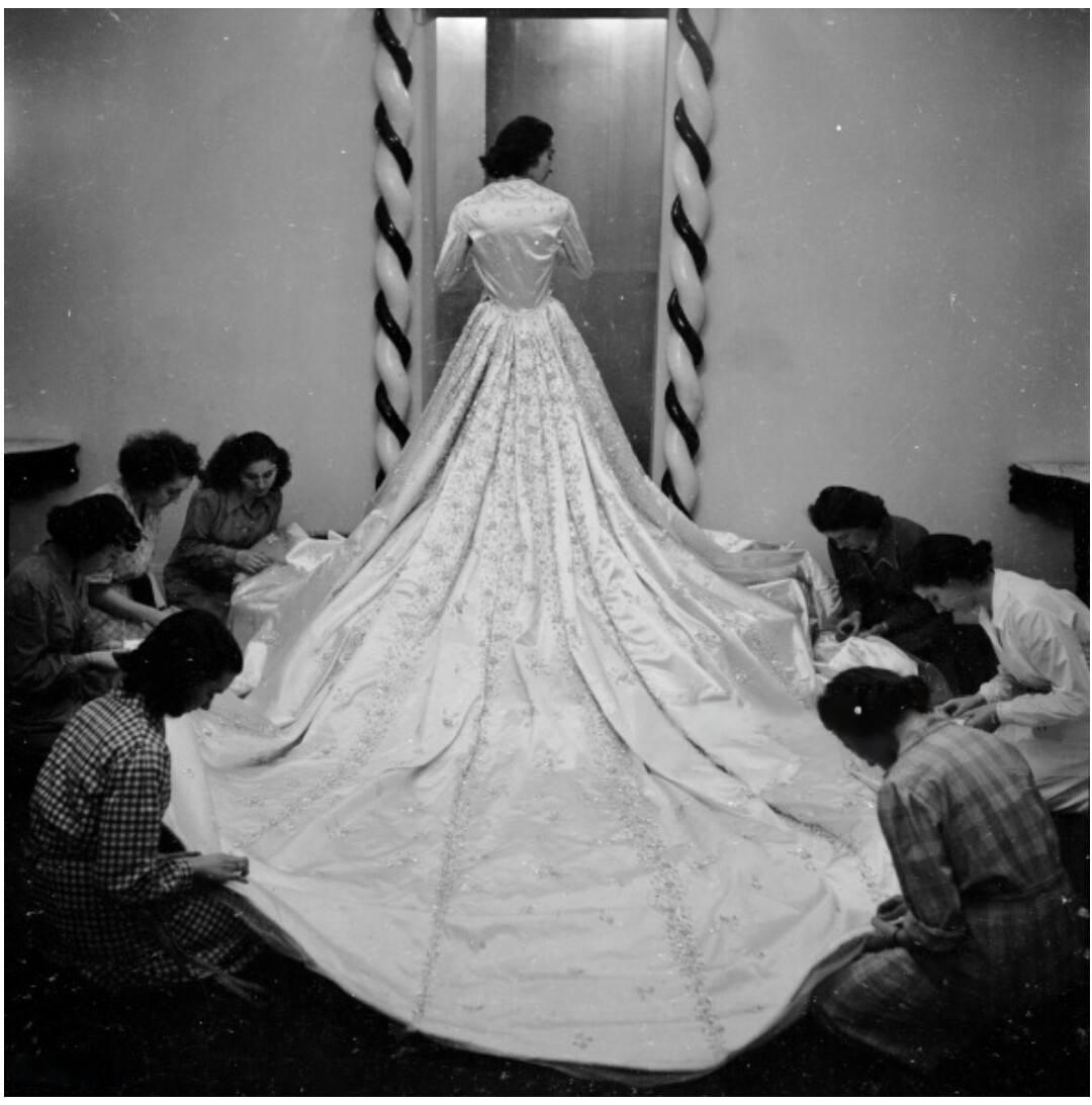 A model wearing Queen Narriman's wedding dress at the atelier while seamstresses finalize it.